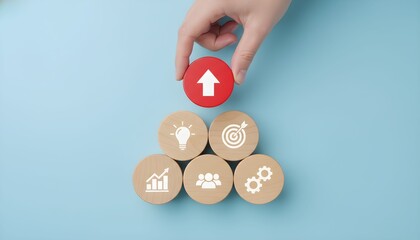 A hand places a red circle with an upward arrow on top of a pyramid of wooden circles with business-related icons, symbolizing growth and success.