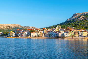 Obraz premium Colorful coastal town with mountains and water under clear blue sky at sunset. Baška, Krk island, Croatia
