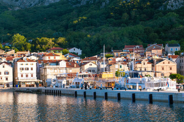 Scenic mediterranean seaside village at sunset with boats and hills. Baška, Krk island, Croatia