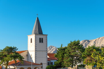 Fototapeta premium Rustic church with steeple and mountain backdrop on a clear day. Baška, Krk island, Croatia