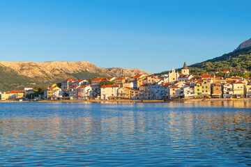Fototapeta premium Scenic coastal town with colorful buildings and mountain views at sunset. Baška, Krk island, Croatia