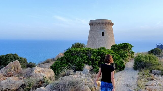Woman walking towards the tower of Les Escaletes, Santa Pola, Alicante, Valencian Community, Spain.