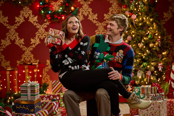 Couple wearing festive ugly Christmas sweaters celebrates the holiday season with wrapped gifts and decorations