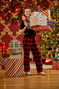 Woman holding wrapped Christmas presents and candy cane decoration in front of decorated holiday tree
