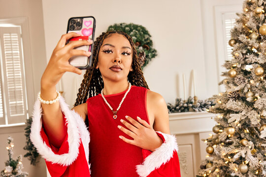 Woman taking selfie in festive red dress with pearl necklace by decorated Christmas tree