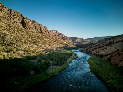River winding through desert canyon landscape with rocky cliffs and green vegetation under clear blue sky - Powered by Adobe