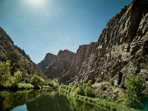 Dramatic canyon walls tower above a tranquil river surrounded by lush green vegetation and rocky cliffs
