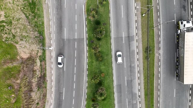 Imagem a&eacute;rea de trecho urbano com pista dupla e canteiro central verde, mostrando circula&ccedil;&atilde;o de ve&iacute;culos, organiza&ccedil;&atilde;o do tr&acirc;nsito e estrutura de mobilidade em &aacute;rea urbanizada