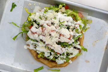 Overhead view of mouth watering Asada Sope meal overloaded with meat, cheese, and lettuce on a tortilla