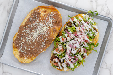 Overhead view of Latino food for a hungry patron includes a huge torta split in halves and loaded with meat and cheese