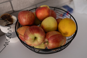 Fresh apples and a lemon arranged in a modern wire fruit basket on a clean kitchen surface, symbolizing healthy living, natural nutrition, and minimalistic home styling for everyday wellness