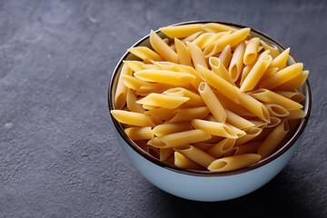 Uncooked Penne Pasta in Bowl on Dark Stone Background Copy Space