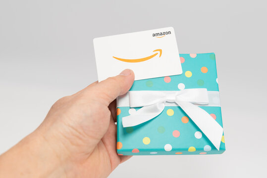 Fuji-shi, Shizuoka-ken - December 30, 2024: Hand holding an Amazon gift card being removed from a polka dot wrapped gift box on a white background. E-commerce shopping concept. Editorial use.