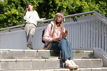 Diverse female students sitting and standing on concrete campus steps with backpack and smartphone