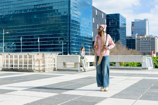 Diverse women walking city plaza with backpack, leaning barrier calling smartphone, copy space