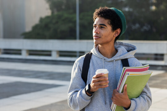 African American male wearing backpack holding folders and coffee cup standing on plaza, copy space