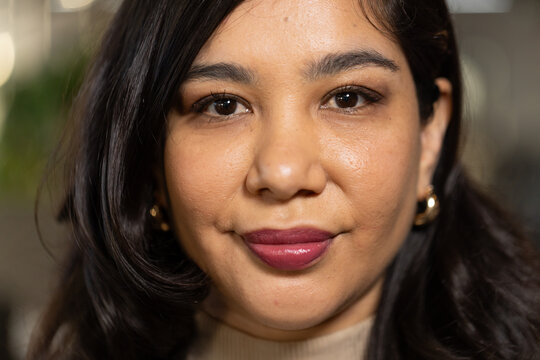 Woman smiling into camera while wearing beige turtleneck sweater and gold hoops at home office