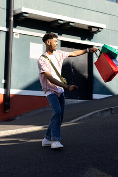 Man walking sloped urban street holding bright shopping bags and wearing crossbody bag, copy space