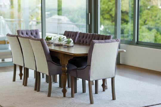 Wooden dining table with eight chairs is resting on rug near windows, displaying glass terrariums