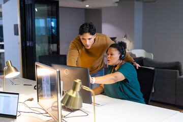 Diverse coworkers collaborating at office desk using computer monitors and headset with brass lamps