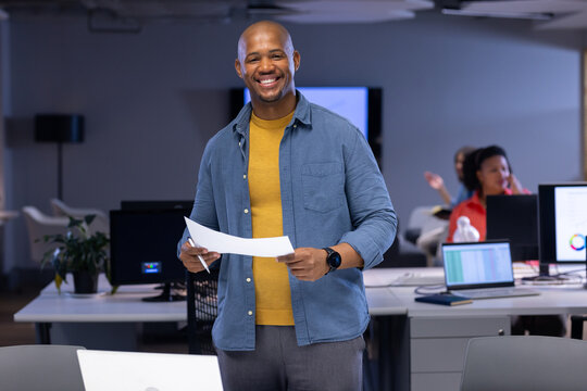 African American male office worker holding documents while standing at desk beside plant