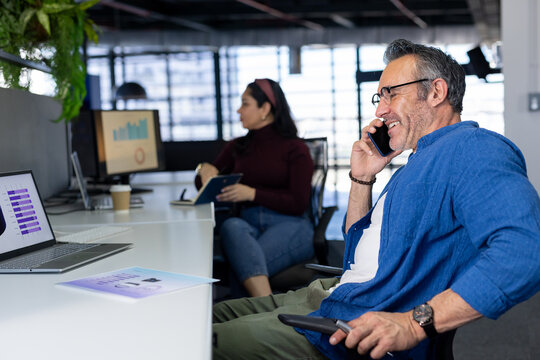 Diverse coworkers talking on smartphone working on laptop in modern office with charts, copy space