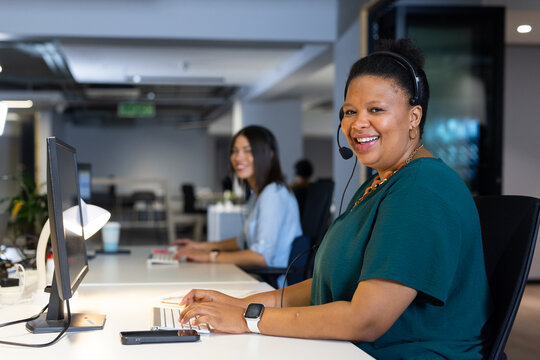 Diverse coworkers typing on keyboards at open-plan office desks with headsets, copy space