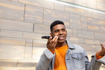 African American man standing on city street holding smartphone near mouth and gesturing