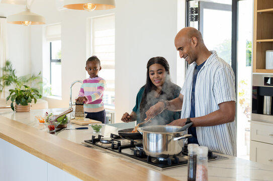 Diverse family cooking on kitchen island in modern kitchen using gas stove while grating vegetables