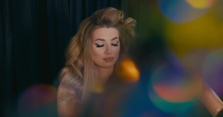Close-up of the face of a blonde girl having her hair adjusted in front of the camera, with a colorful glass object blurred in the foreground. - Powered by Adobe