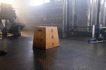 Wooden plyo box sitting on rubber floor, stenciled heights, kettlebells, squat rack, sun streaming