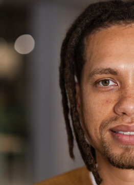 Right half male face is making eye contact and smiling in studio, dreadlocks, mustard-brown top