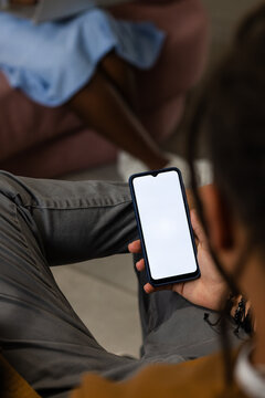 Smartphone is resting on gray pants with black case and blank screen in lounge, blurred sofa