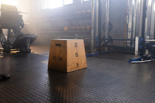 Wooden plyo box sitting on rubber floor, stenciled heights, kettlebells, squat rack, sun streaming