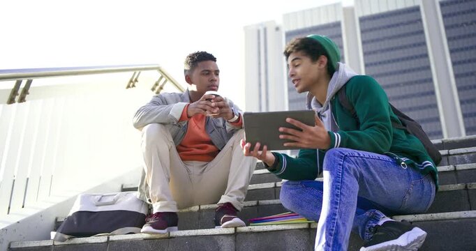 Diverse male friends unfolding tablet, tapping screen, holding coffee and studying on campus steps