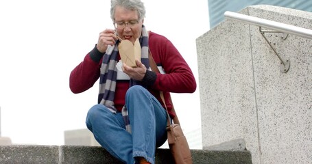 Middle-aged male sitting on stair wearing striped scarf eating takeout with chopsticks, copy space - Powered by Adobe