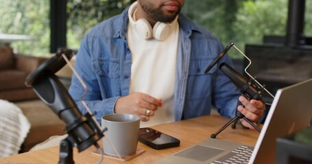 African American man typing on laptop and adjusting mic, headphones in home studio preparing stream - Powered by Adobe