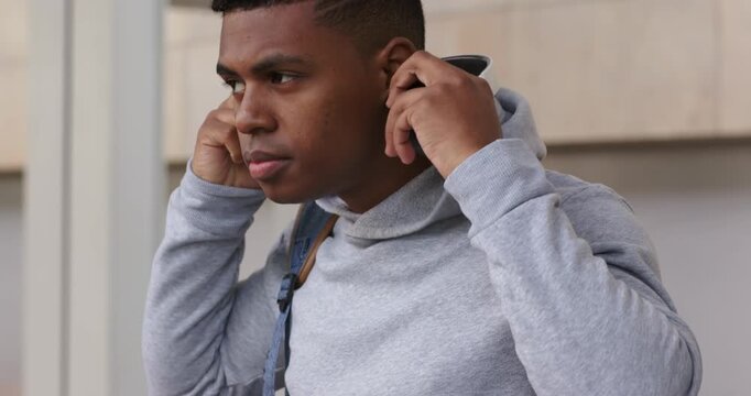 African American man adjusting hoodie lifting headphones over ears by stone facade, preparing audio