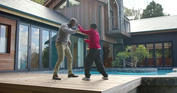 African American father and son stepping onto deck practicing boxing poolside and sharing high-five