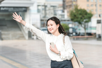 A young Asian businesswoman raising her hand to hail a taxi at a taxi stand (business...