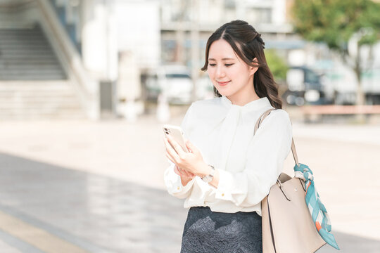 A woman using a smartphone at a station rotary (app, mobile ticket, ticketless, electronic ticket)
