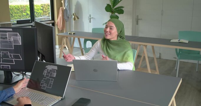 Diverse coworkers reviewing floorplans in studio after laptop tap, noting design ideas