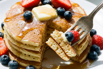 Breakfast with pancakes with butter, honey, strawberries, and blueberries