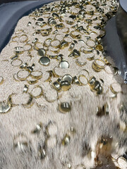 Deburring process for brass parts, drying in corn sawdust, dynamic close-up of small golden metal parts tumbling in industrial polishing media