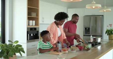 Gathering around kitchen island Black family grating carrot slicing cucumber stirring veg for salad
