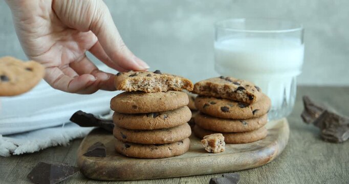 Woman breaking chocolate chip cookie at wooden table, closeup