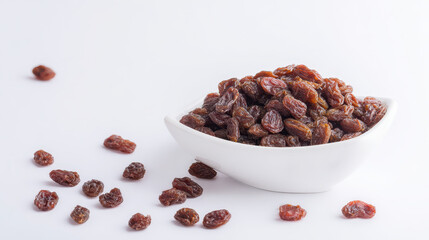 Fototapeta premium Dried raisin fruit in white bowl with scattered raisins on white background, healthy snack with natural sweet flavor and chewy texture