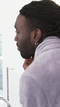 Vertical video: Entering bathroom to groom, man in bathrobe using shaver, applying cream