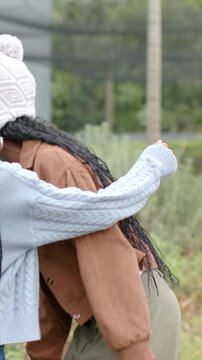 Vertical video: Answering call, sisters in pompom hats hugging in yard, raised bed