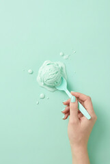 A minimal mint-green flat lay featuring a hand holding a spoon with melting mint ice cream on a matching pastel background